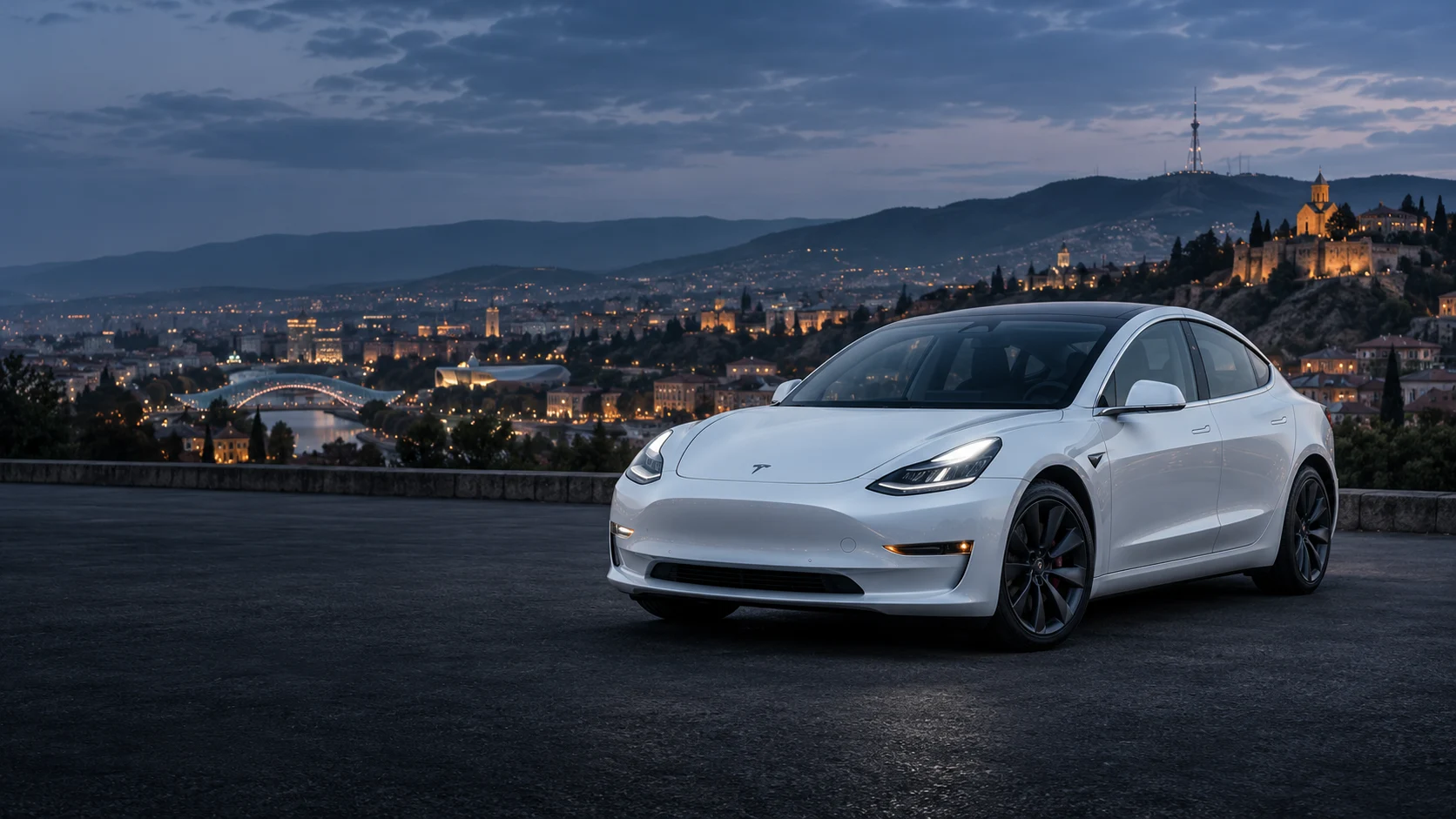 თეთრი Tesla Model 3 თბილისის საღამოს ხედის ფონზე